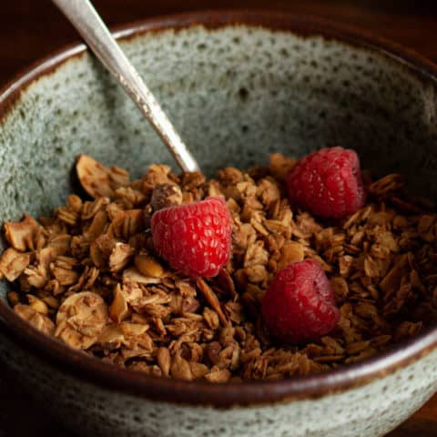 Granola in blue speckled pottery bowl with raspberries on top