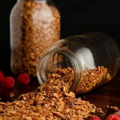 Homemade Granola in 2 canning jars spilling on table with raspberries