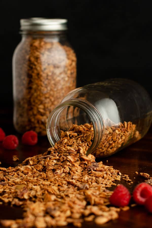 Homemade Granola in 2 canning jars spilling on table with raspberries