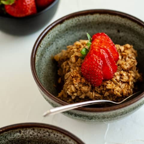 Baked oatmeal in a blue pottery bowl topped with a strawberry