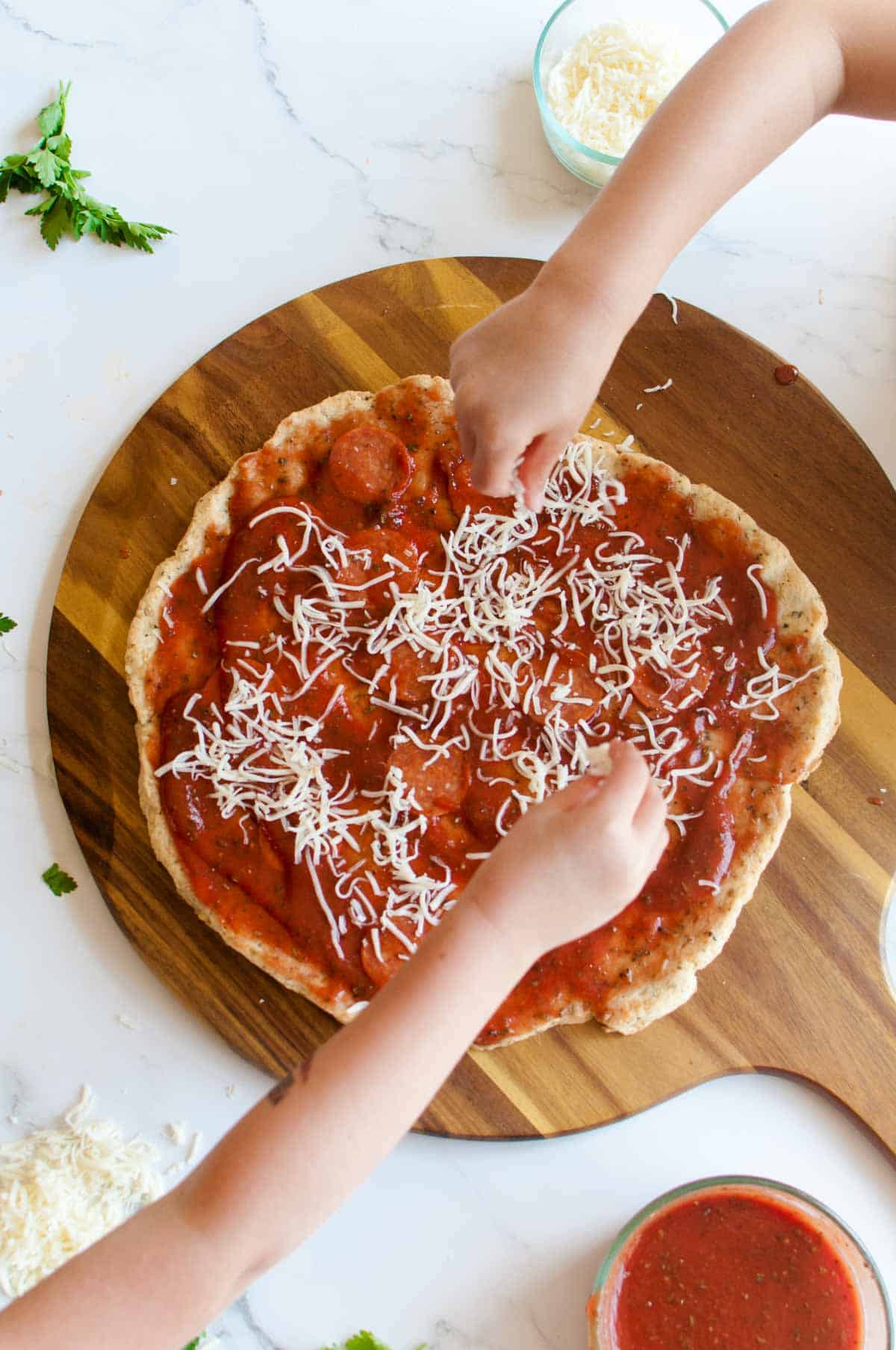 Gluten Free No Yeast Pizza Crust with childrens hands in the scene applying toppings