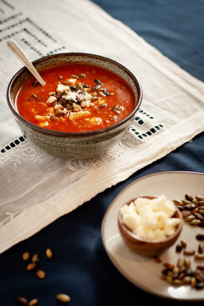 Roasted Red Pepper soup on lace cloth sith pumpkin seeds and feta crumbles