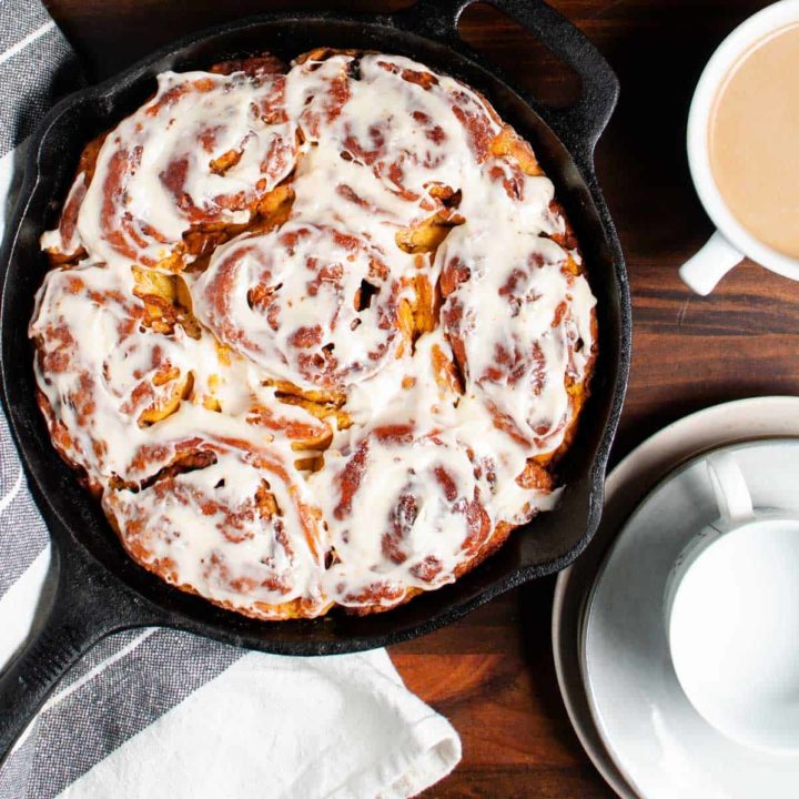 gluten free pumpkin cinnamon rolls displayed in a cast iron skillet ready to serve with coffee