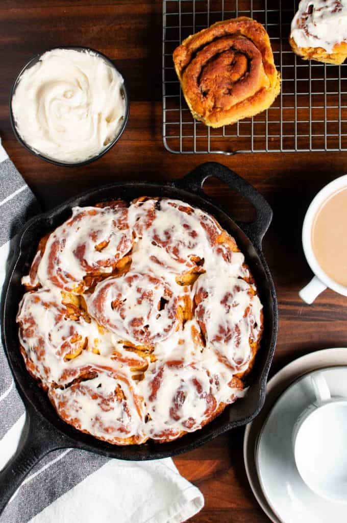 gluten free pumpkin cinnamon rolls displayed in a cast iron skillet ready to serve with coffee