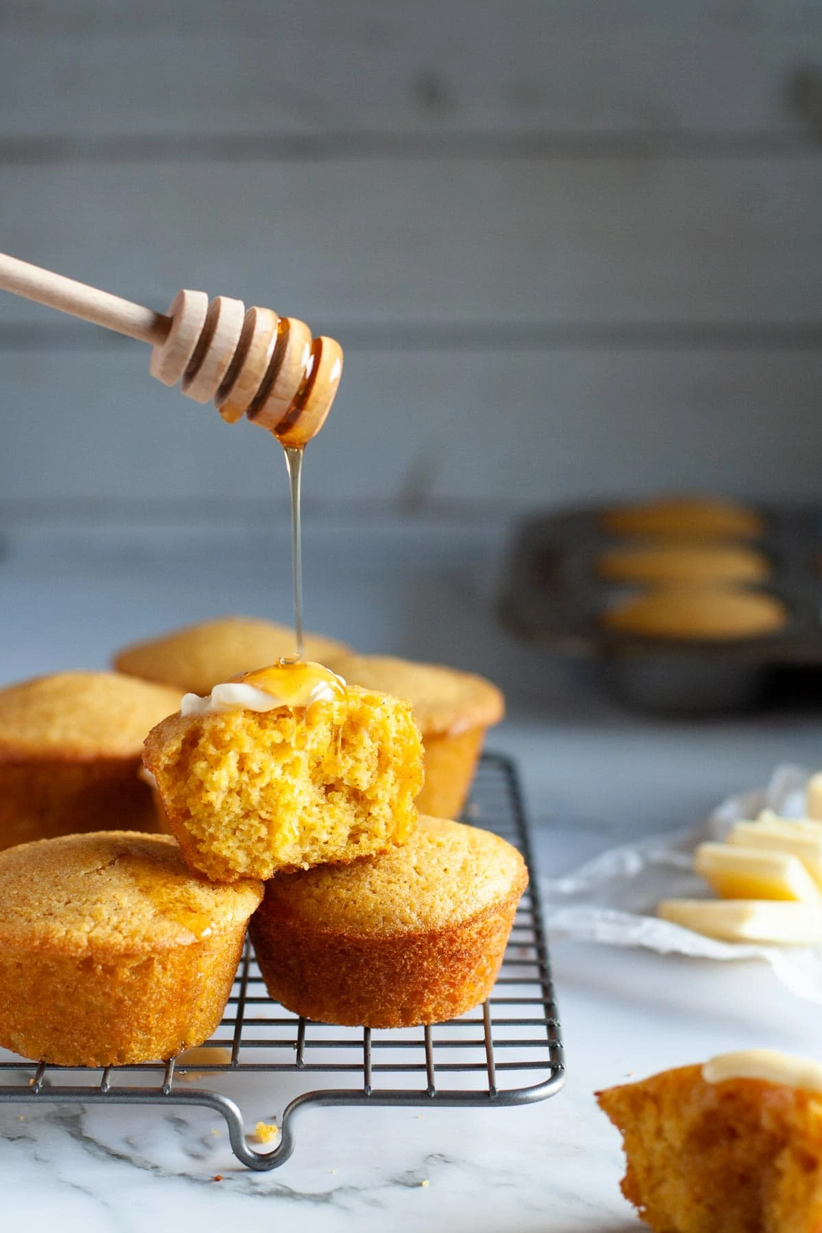 honey dropper drizzling a stream of honey on cornbread muffins