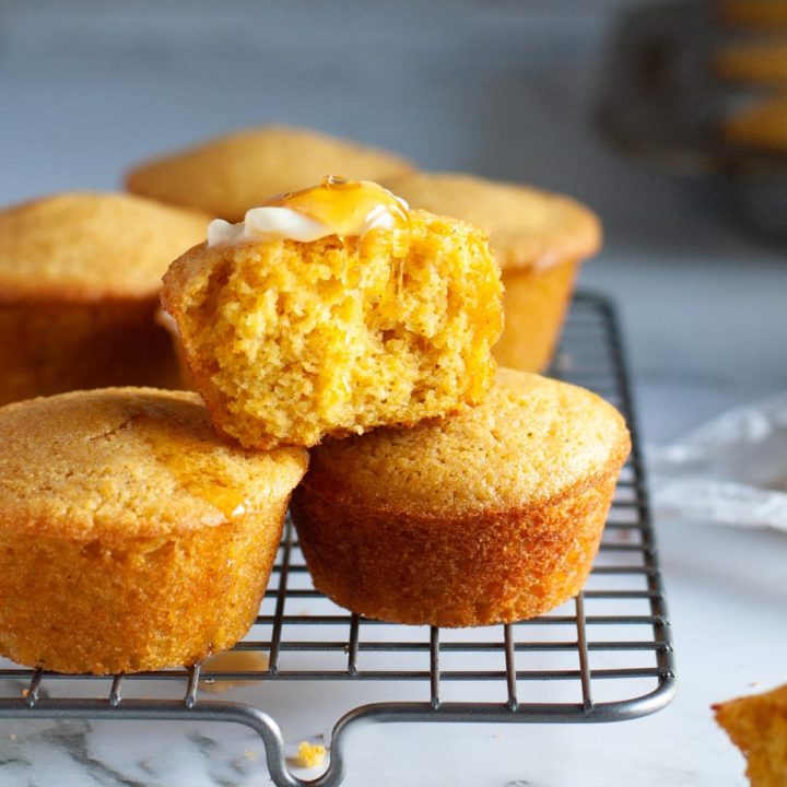 cornbread muffins stacked on cooling rack with butter and honey drizzling down top.