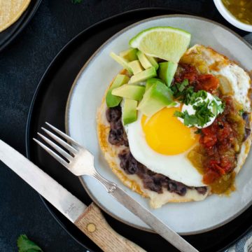 easy huevos rancheros on ceramic plate ready to eat and topped with salsas, avocado and lime