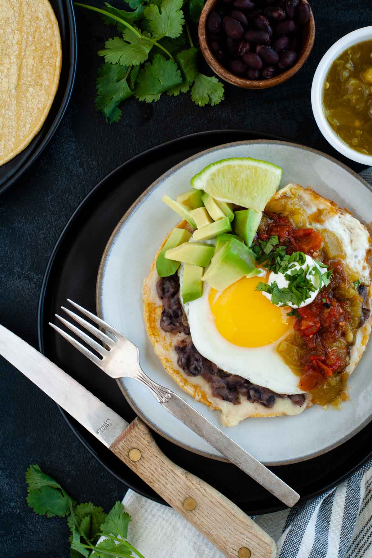 easy huevos rancheros on ceramic plate ready to eat and topped with salsas, avocado and lime