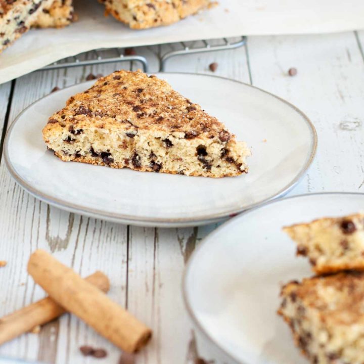 recipe card image for gluten free cinnamon scones, scone slice displayed on glass plate sitting on white wooden surface