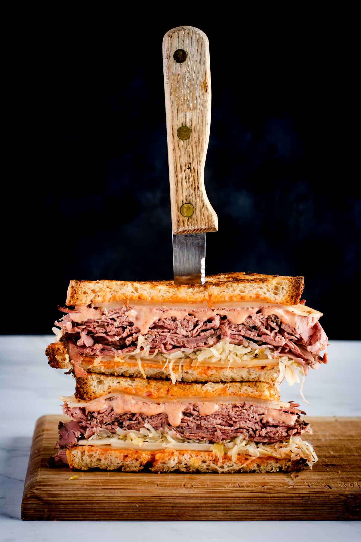 corned beef sandwich with russian dressing displayed on a cutting board, two stacked halves with a steak knife through them.