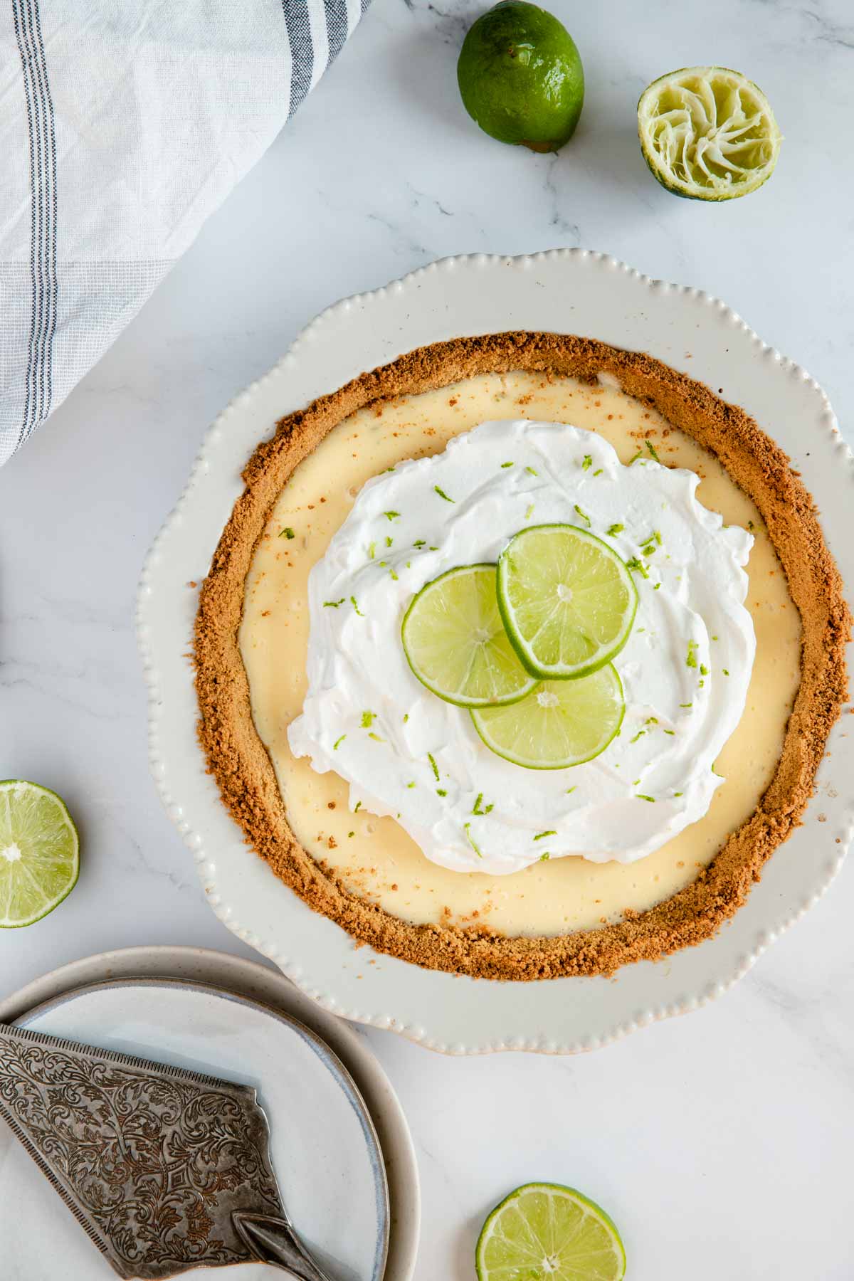 gluten free key lime pie ready to be served, surrounded by limes and serving dishes.