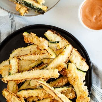 Oven baked zucchini fries served on a black plate with dipping sauce next to them