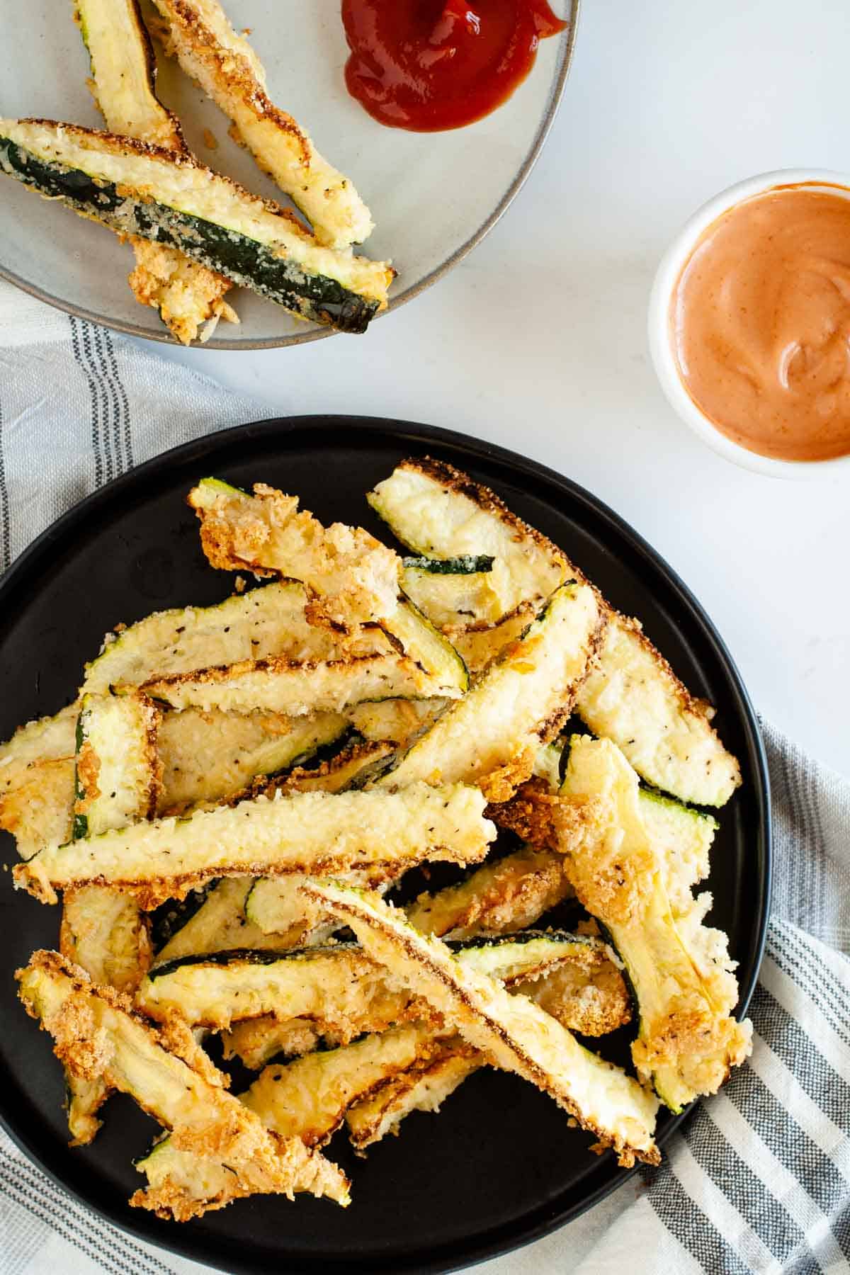 Oven baked zucchini fries served on a black plate with dipping sauce next to them