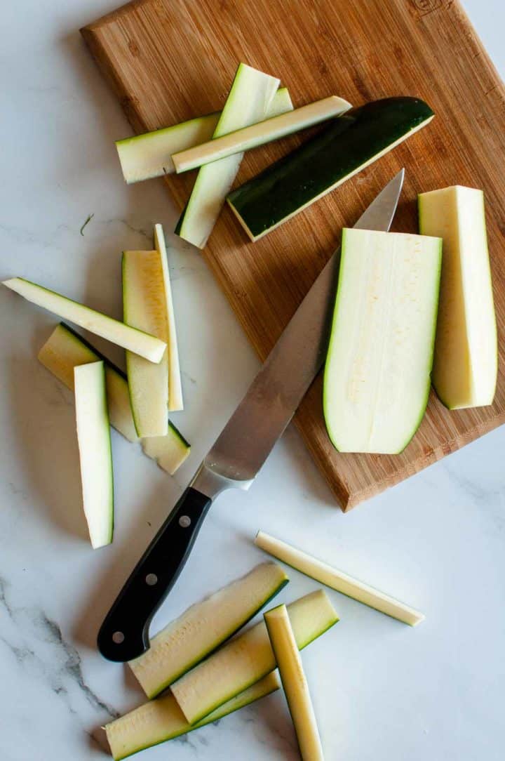 step photo for how to cut zucchini sticks, zucchini slices on a cutting board with knife