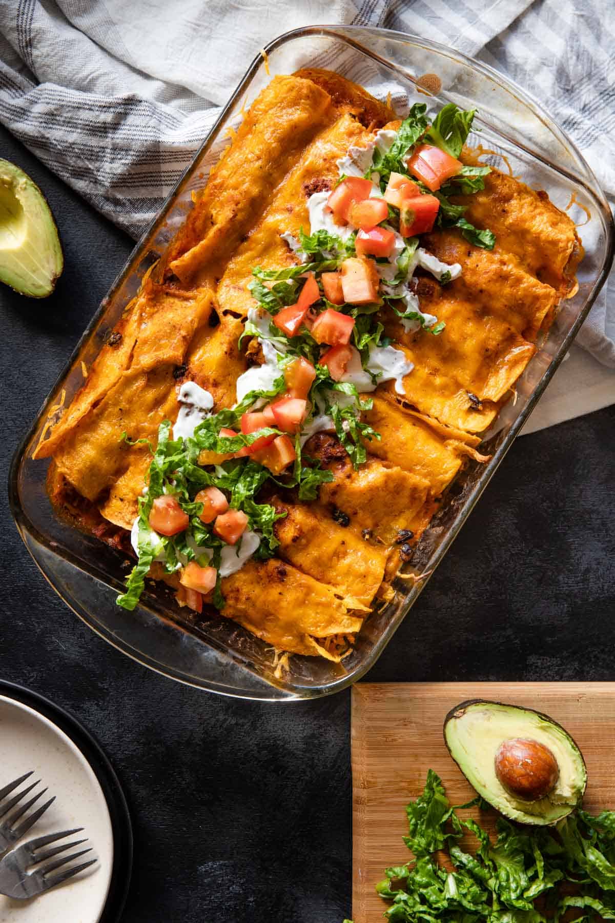 the cooked finished baking dish of gluten free chicken enchiladas ready to be served and topped with sour cream, lettuce and tomato