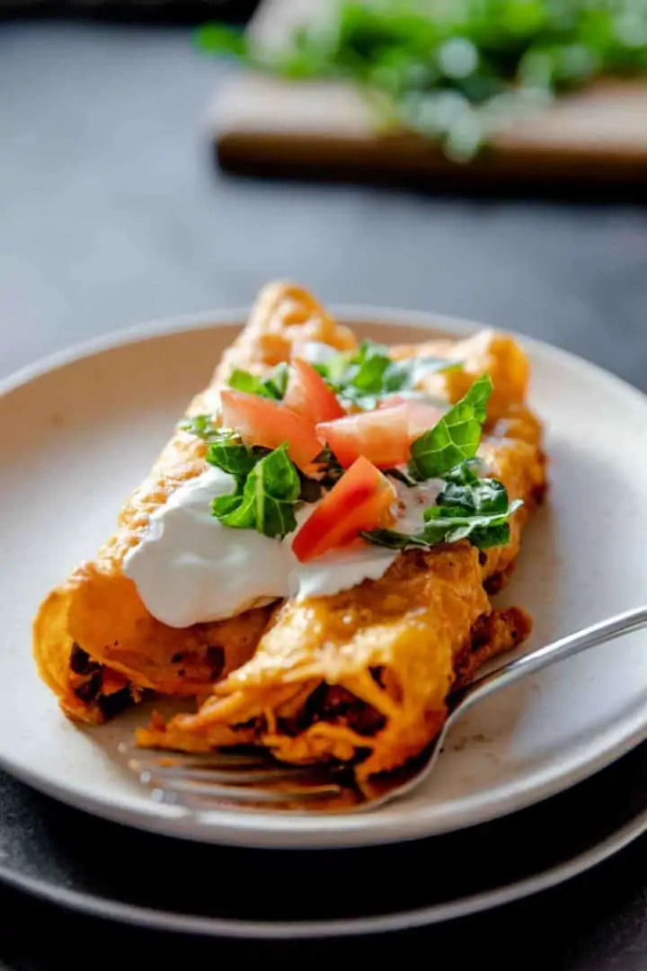 serving of gluten free chicken enchiladas ready to be eaten and served with lettuce, tomato and sour cream