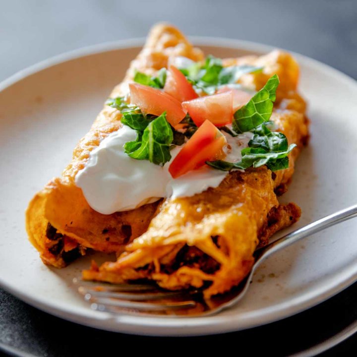 individual serving of gluten free chicken enchiladas cooked and served with sour cream, lettuce and tomato