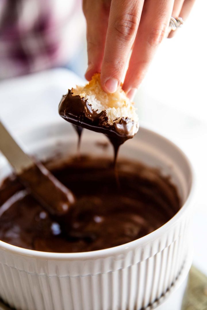 chocolate dripping from the bottom of a coconut macaroon as it is being dipped and pulled from the chocolate