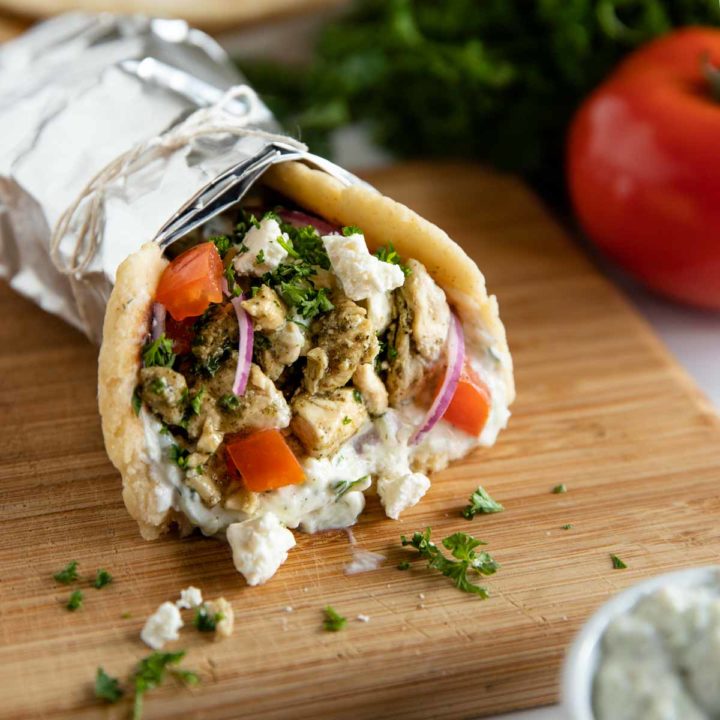 chicken gyro wrapped in foil and ready to eat, sitting on a cutting board and surrounded by fresh ingredients.