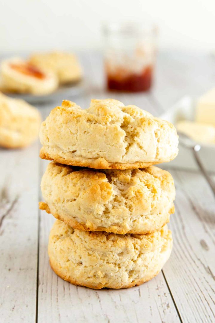 3 gluten free biscuits stacked on top of each other with butter and jam in the background