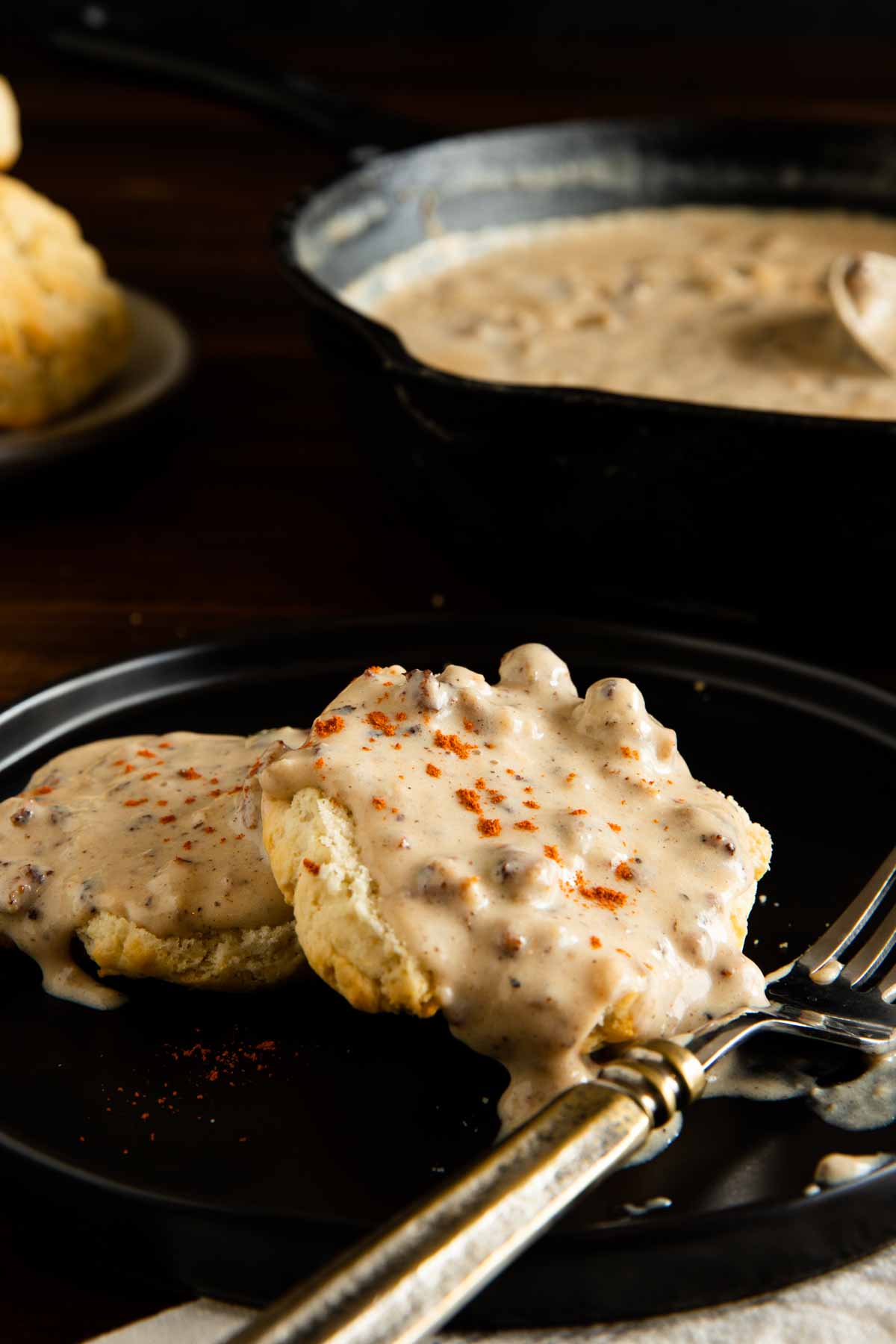 gluten free sausage gravy served over a biscuit and served on a black plate with a sprinkle of paprika