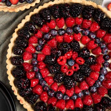featured image of white chocolate berry tarts with different berry options. Large tart featuring circles of raspberries, and blackberries, smaller tart featuring spirals of strawberries and blueberries