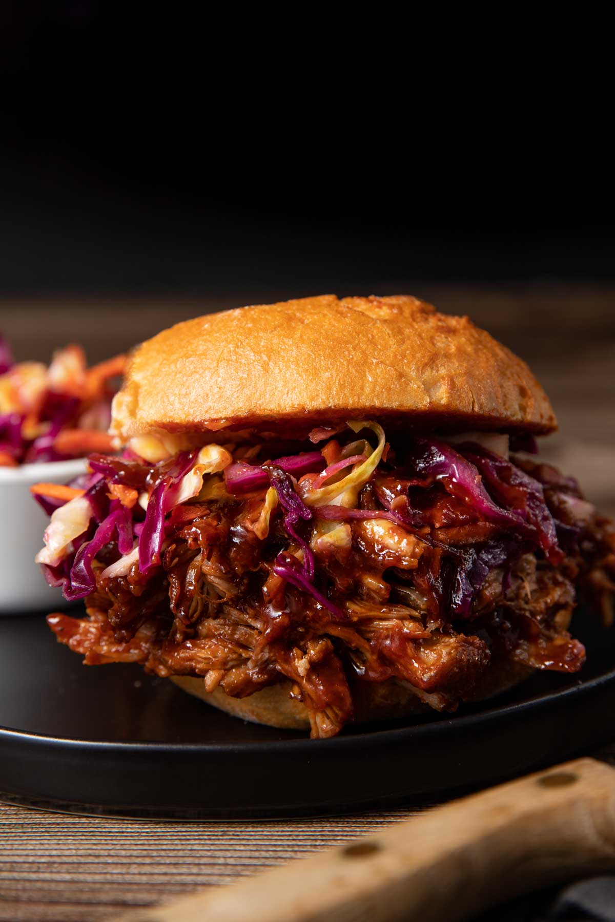 homemade pulled pork with a bun and topped with a serving of coleslaw, served on a black plate