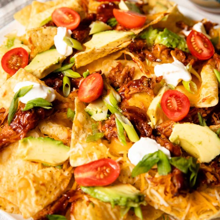 close up of pulled pork nachos served with tomatoes, onion, avocado and sour cream