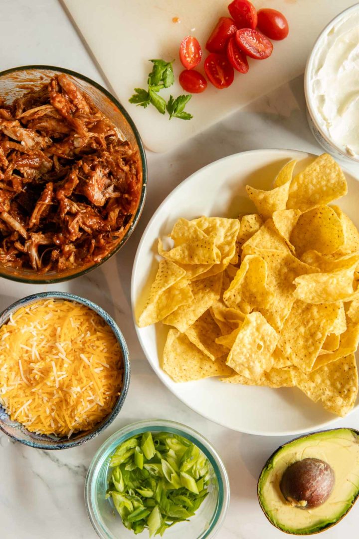 Photo of ingredients needed for shredded pork nachos, chips, pulled pork, shredded cheese and desired toppings