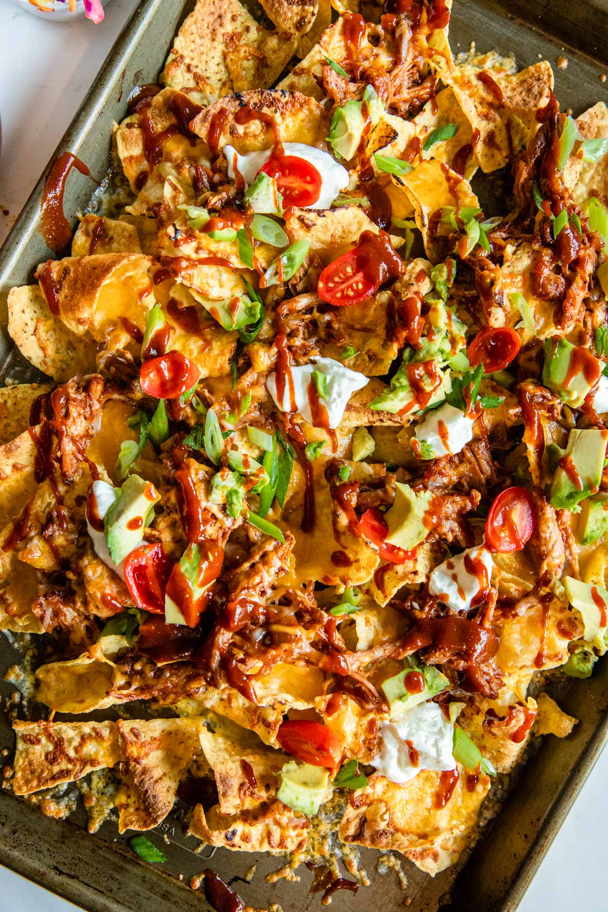 bbq pulled pork nachos fresh from the oven on a baking sheet topped wit toppings